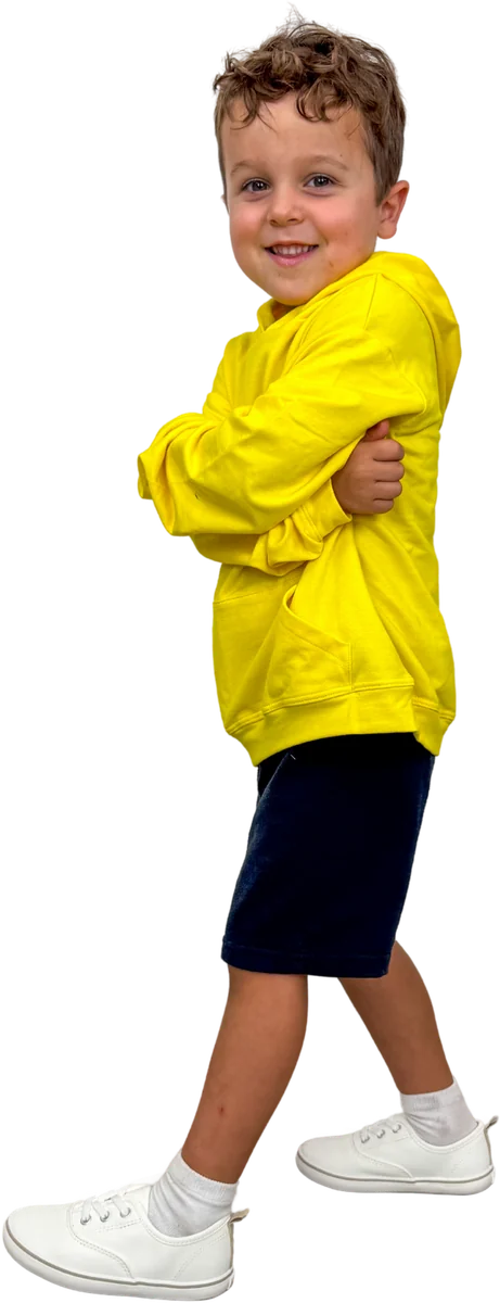 Young boy in a yellow hoodie and navy shorts, smiling with his arms folded